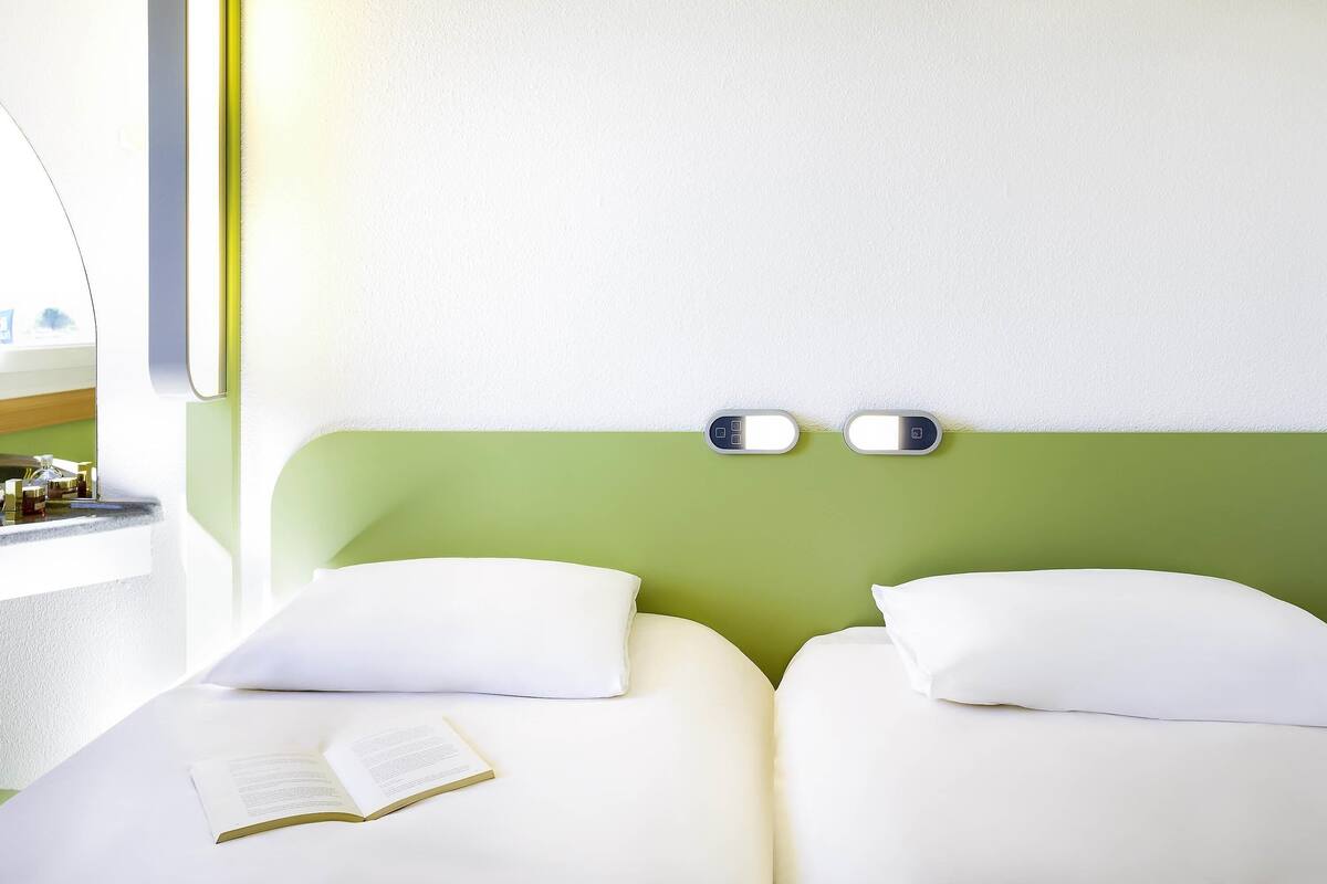 Une chambre d’hôtel avec un lit, des oreillers, une table de chevet, un miroir et une fenêtre.