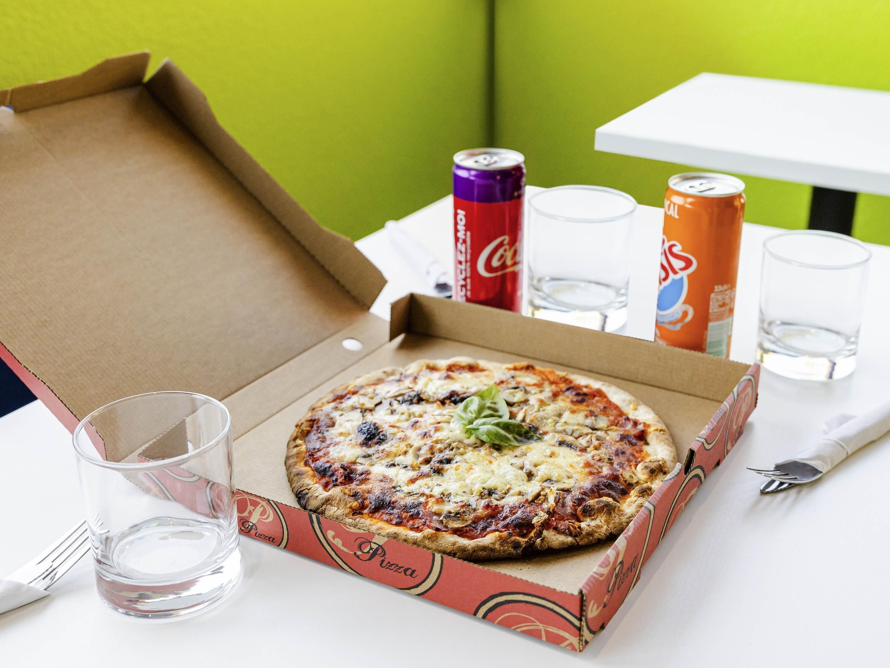 A pizza box with a pizza on a table, a fork, a knife, and two glasses.