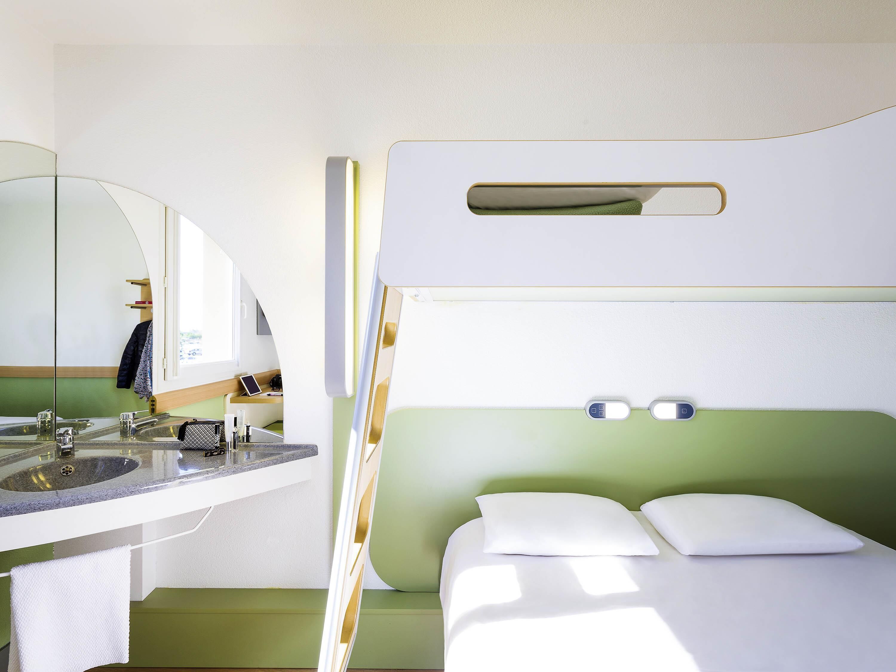 Une chambre compacte et moderne, équipée d’un lit superposé, d’un petit lavabo et d’un miroir.