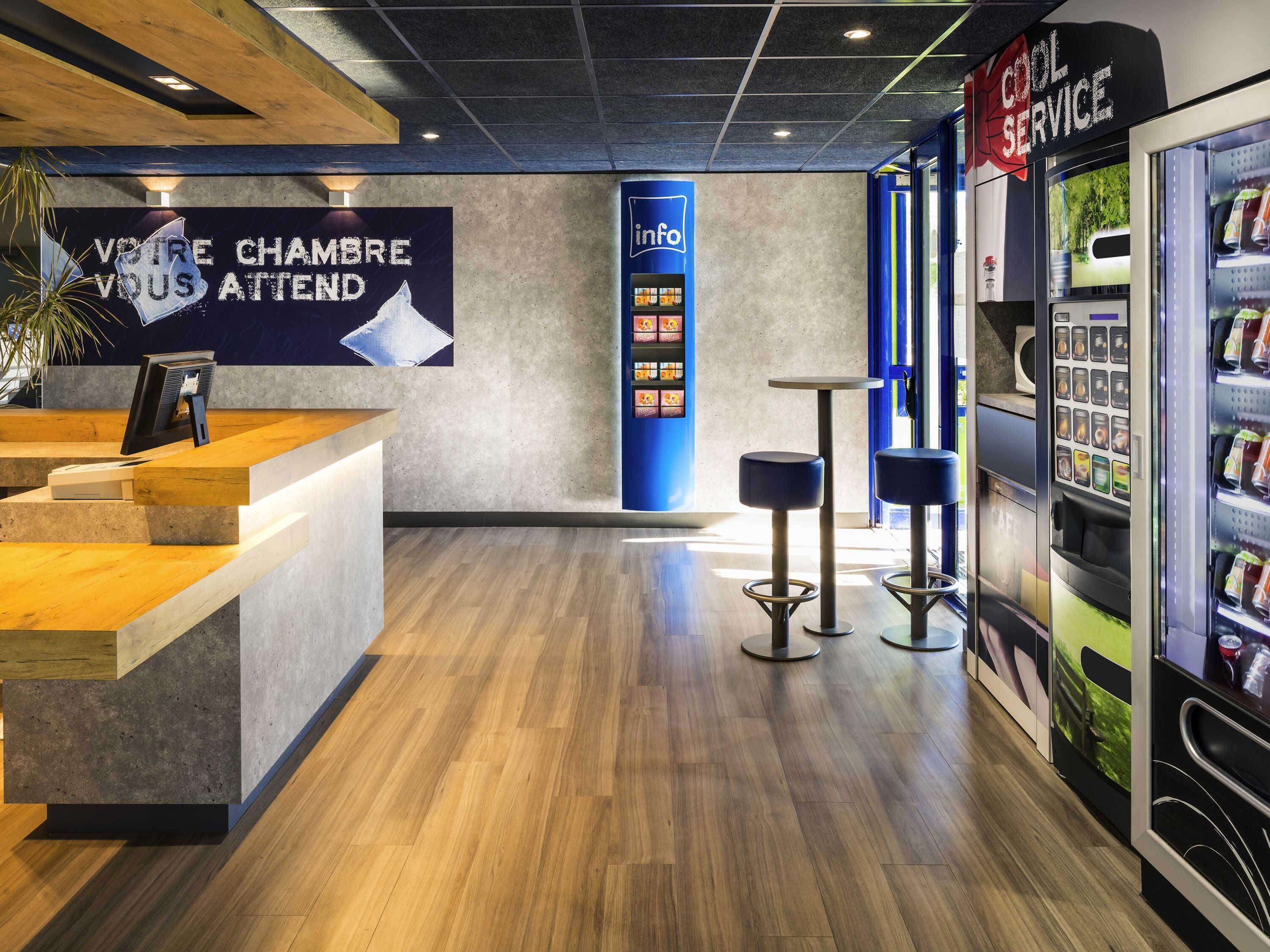 A modern reception area with a wooden reception desk, a digital information kiosk, and a vending machine.