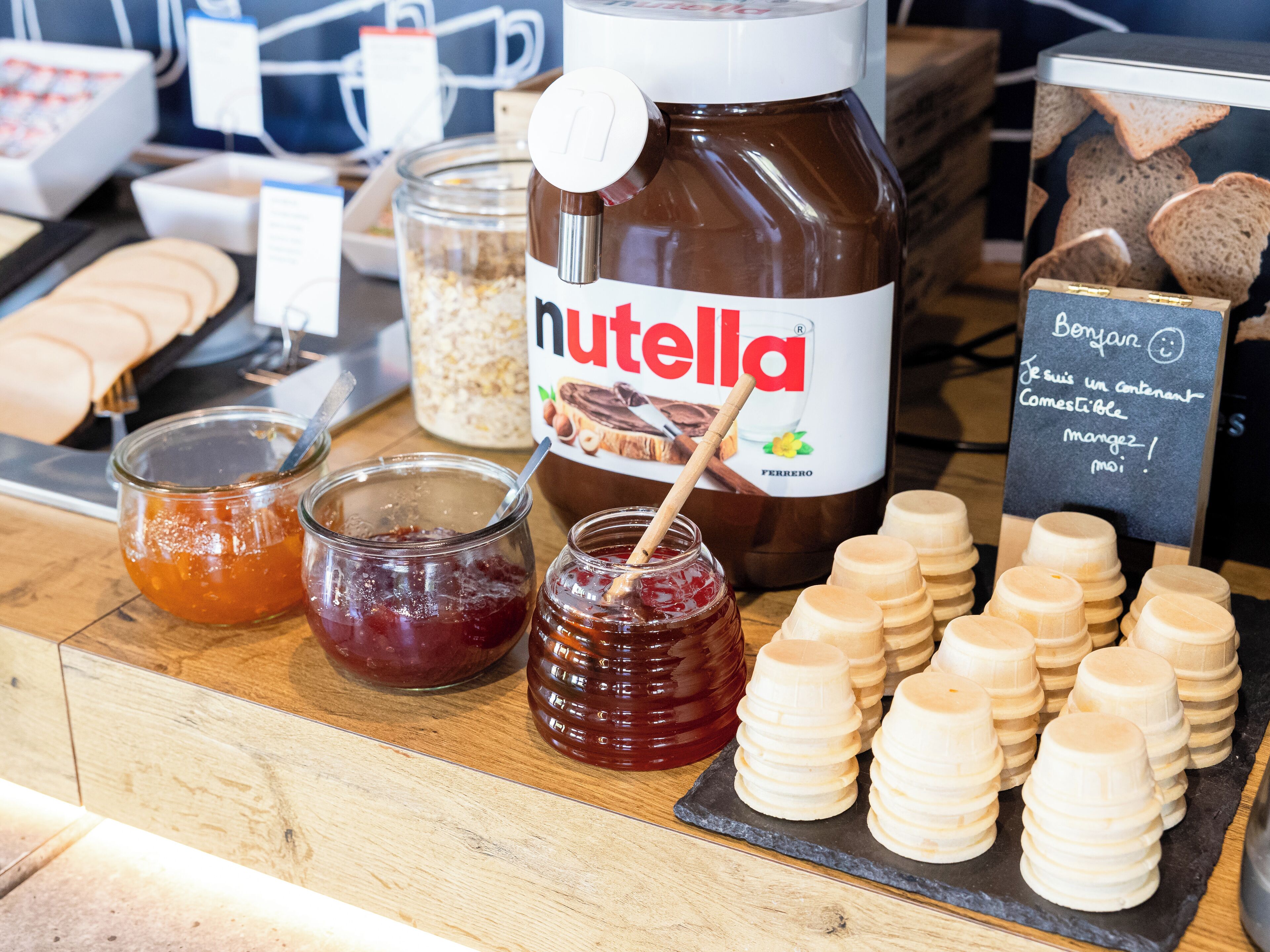 A display of Nutella, jars of jam, and wooden cups on a counter.