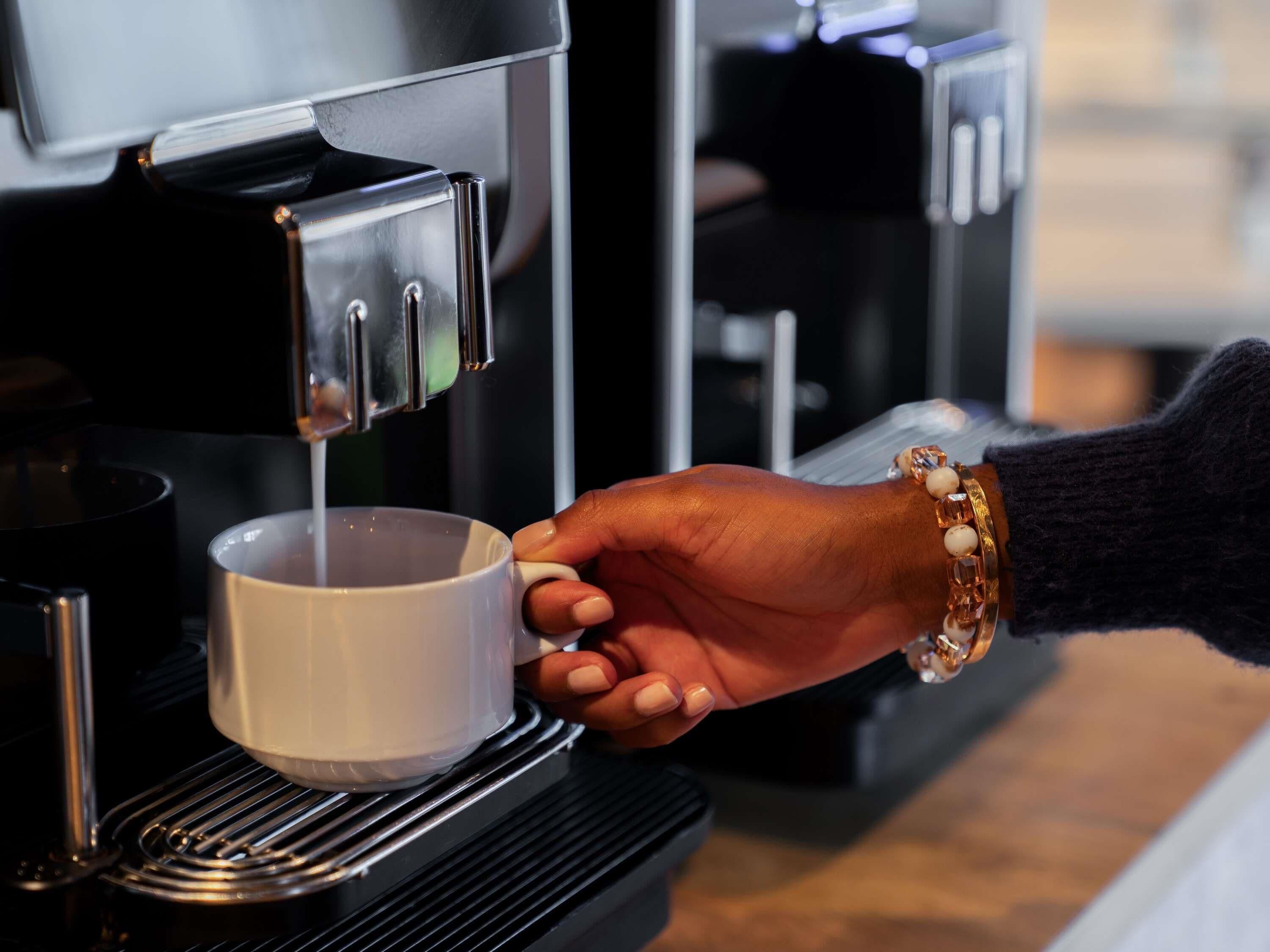 Una mano sostiene una taza debajo de una máquina de café.