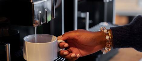 Una mano sostiene una taza debajo de una máquina de café.