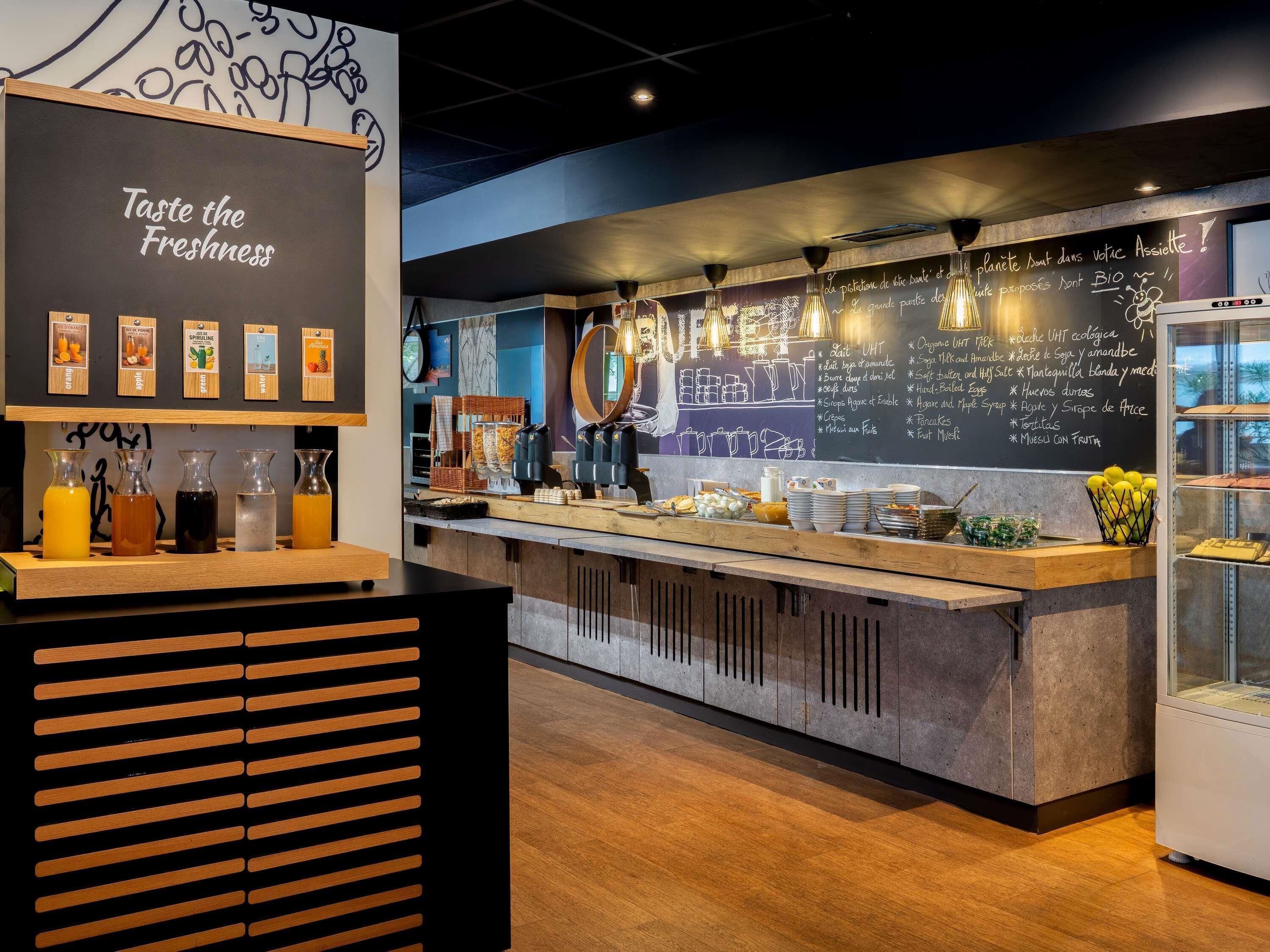 Una cafetería con un menú en una pizarra, una exhibición de jugos y una barra con diversos alimentos.