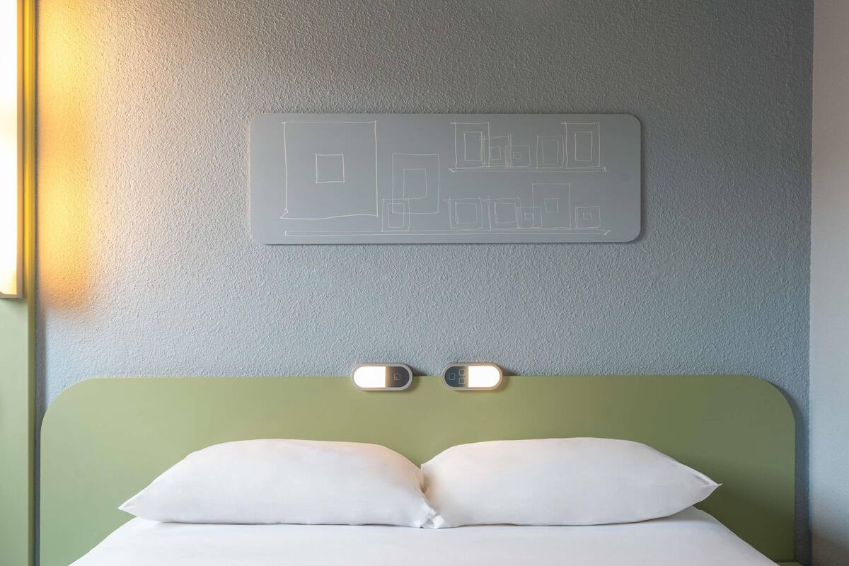 A bed with a green headboard, two bedside lamps, and a wall-mounted light fixture.