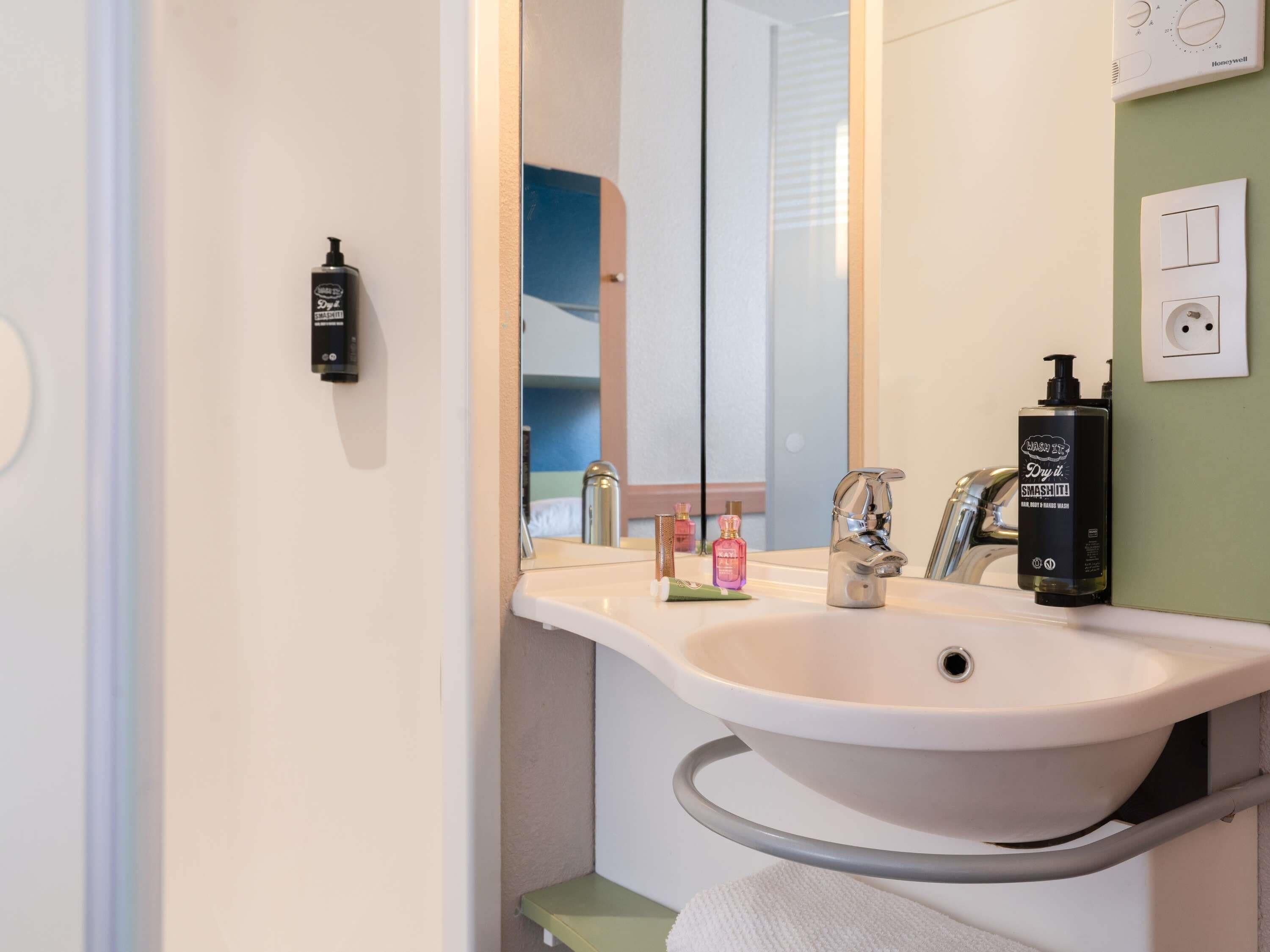 A bathroom with a white sink, a mirror, a handheld showerhead, and toiletries.