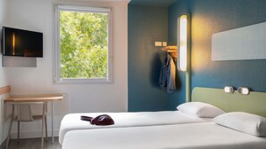 Hotelkamer met een bed, bureau, stoel, televisie en raam met uitzicht op bomen.