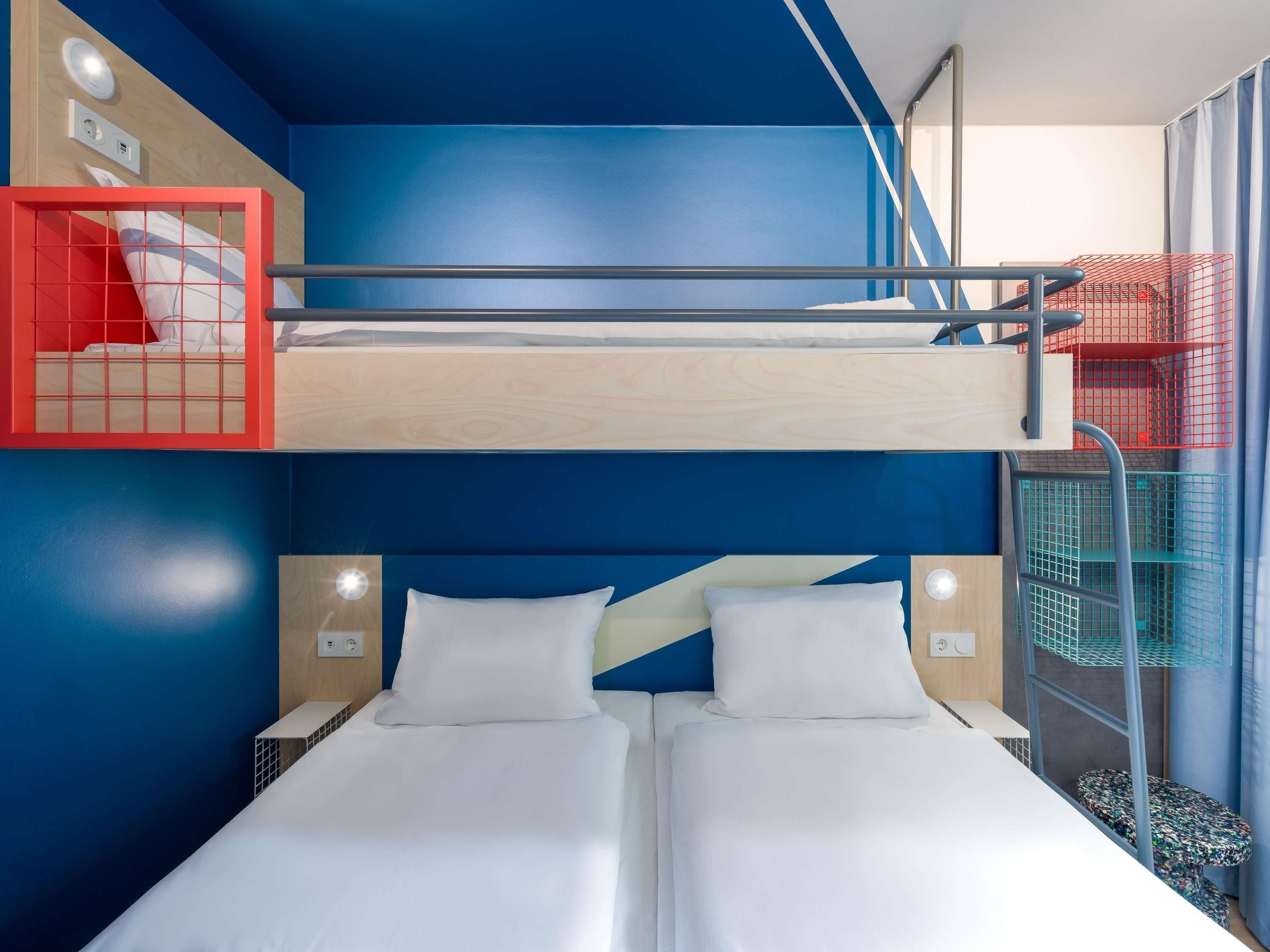 A bunk bed with two beds, a red storage unit, and a small table with a patterned top.