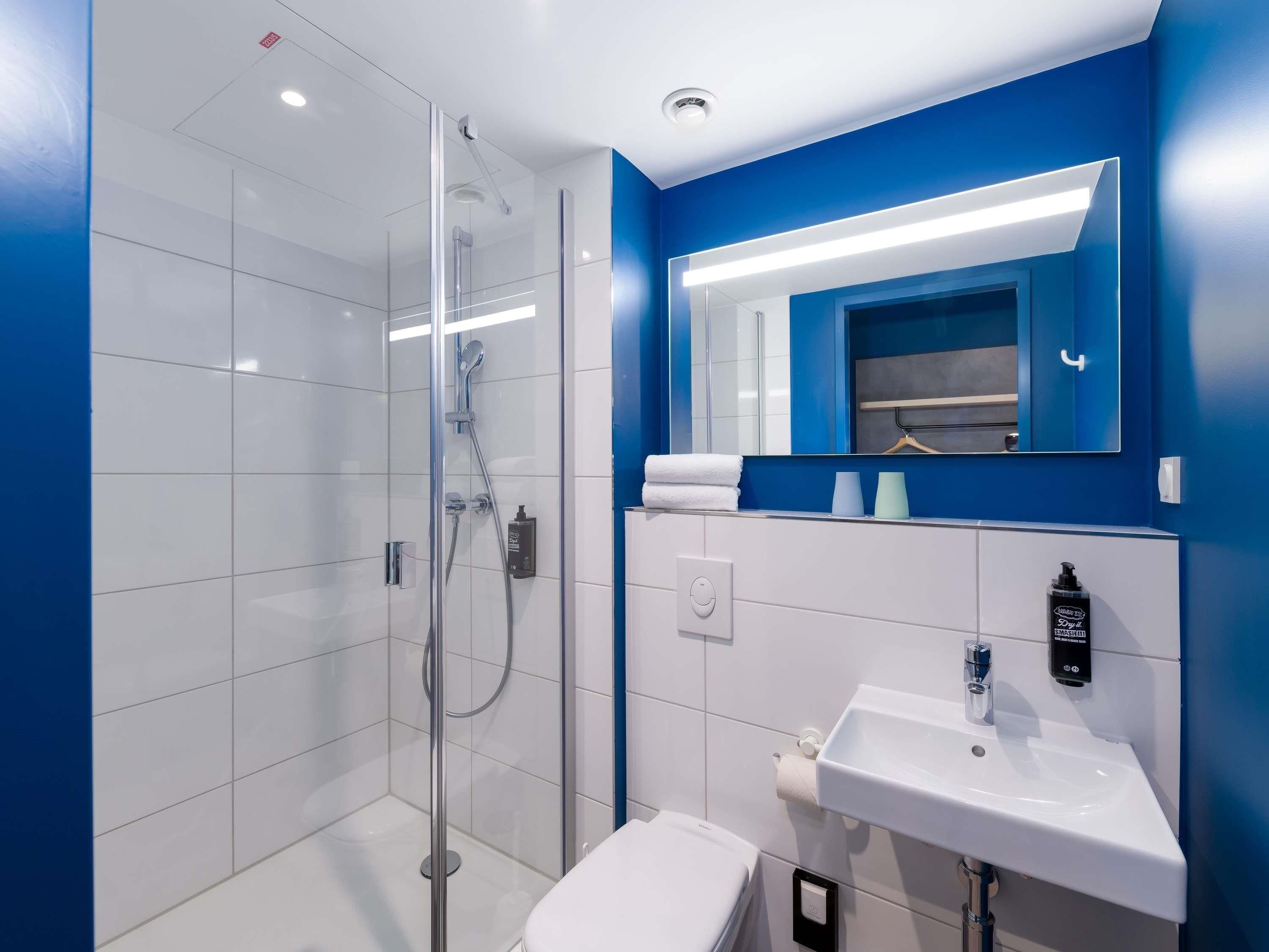 Un bagno moderno con doccia vetrata, lavandino bianco e uno specchio su una parete azzurra.
