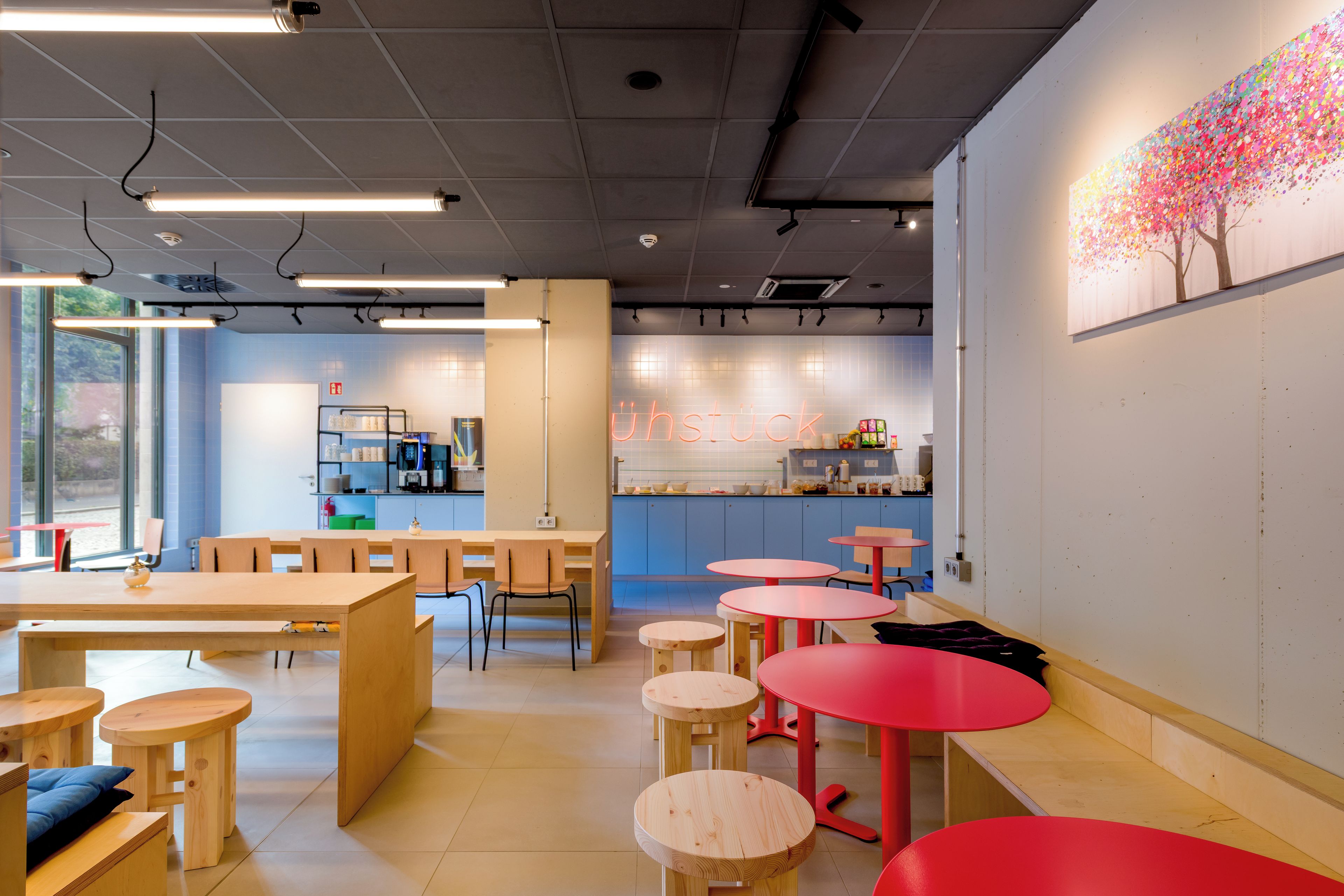 Ein modernes Café-Interieur mit Holztischen und -stühlen, einer Küchenzeile und einem an der Wand hängenden Gemälde.