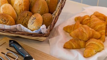 A basket of bread rolls and croissants on a table.