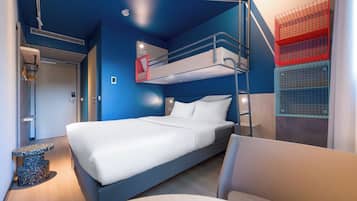 Ein Stockbett mit weißer Matratze und Kissen, ein Schreibtisch mit Stuhl und ein rotes Staufach an der Wand.