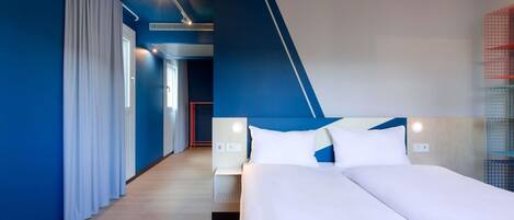 A modern hotel room with a large bed, a bedside table, a nightstand, and a built-in heater.