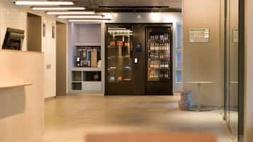 Een moderne lobby met een koffieapparaat, automaat en een glazen wand.
