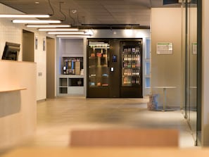 A modern lobby with a coffee machine, vending machine, and a glass wall.