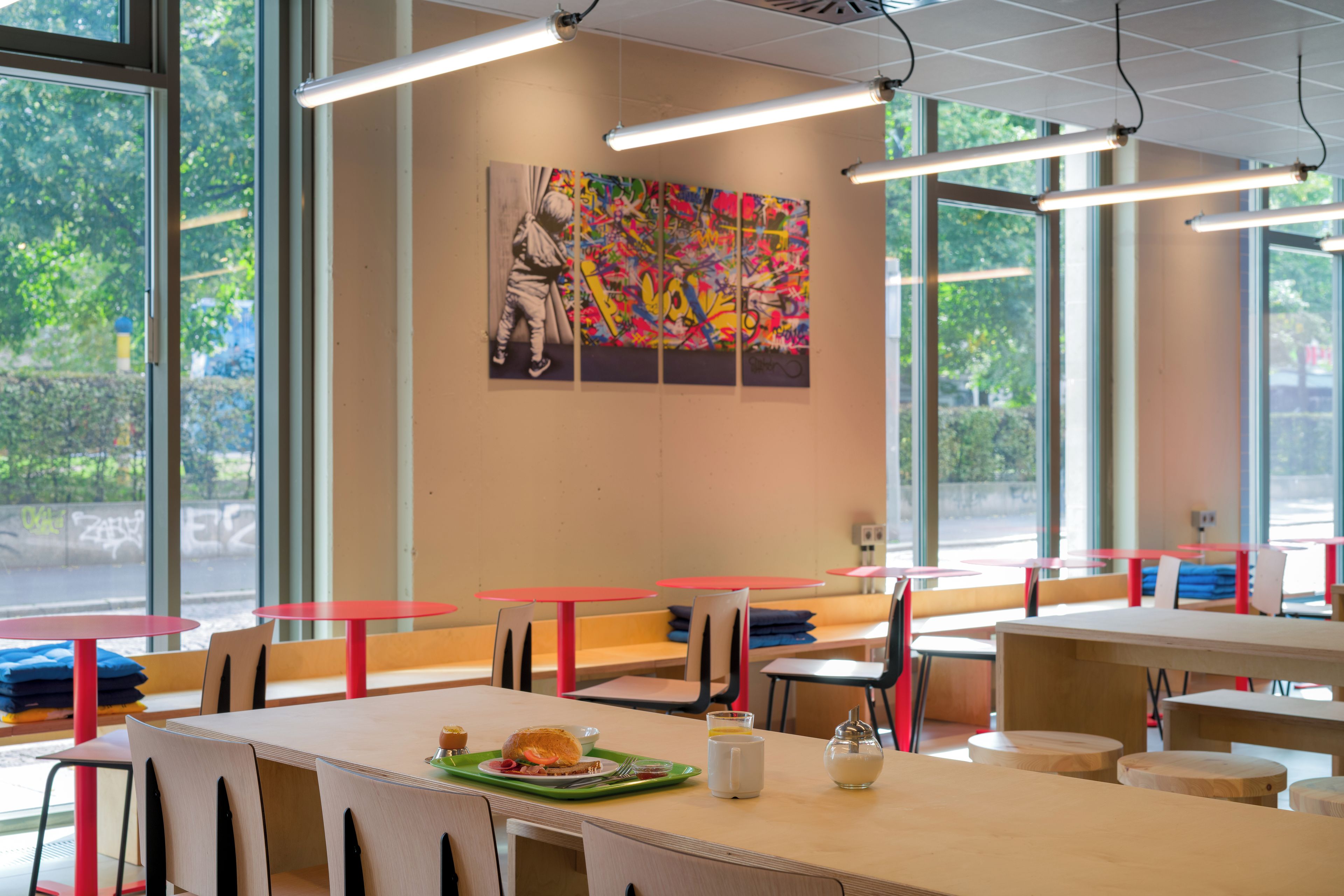 A dining area with tables and chairs, artwork on the wall, and large windows.