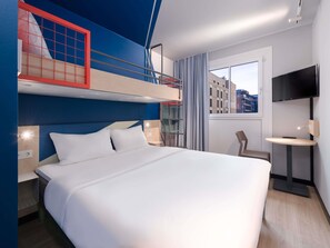 Habitación de hotel con literas, televisor de pantalla plana, mesita de noche y ventana con vista a la ciudad.