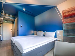 Una habitación de hotel moderna con una cama grande, una pared de acento azul y un estante empotrado con cestas de almacenamiento.