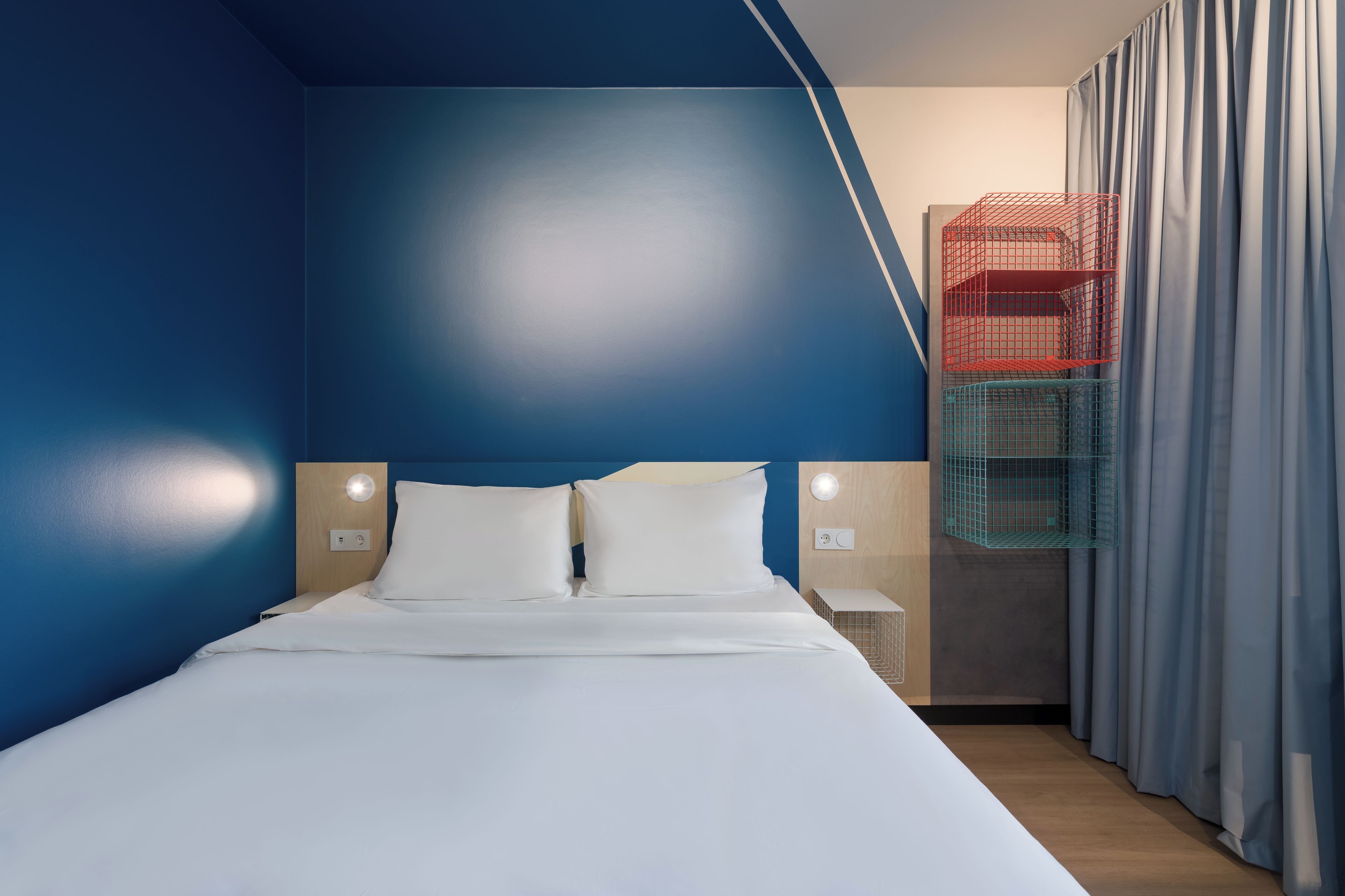 Une chambre d’hôtel moderne avec un grand lit, deux tables de chevet et un placard intégré doté de rangements rouges et verts.