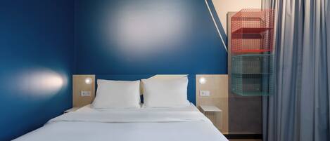 Quarto de hotel moderno com uma cama grande, duas mesas de cabeceira e um guarda-roupa embutido com compartimentos de armazenamento em vermelho e verde.