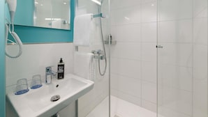 A modern bathroom with a white sink, a mirror, a hairdryer, and a glass shower enclosure. - ibis budget Leipzig City (Leipzig)