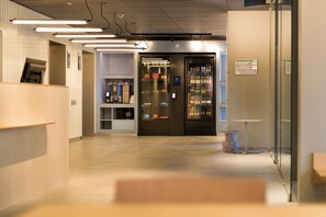 A modern interior with a vending machine, a coffee machine, and a seating area. - ibis budget Leipzig City (Leipzig)