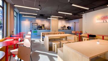 A modern interior with multiple tables and chairs, a kitchen area, and large windows allowing natural light.