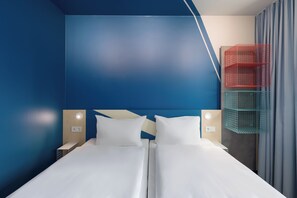 Una cama doble con ropa blanca, dos mesitas de noche con lámparas y un mueble de almacenamiento rojo y verde fijado a la pared.