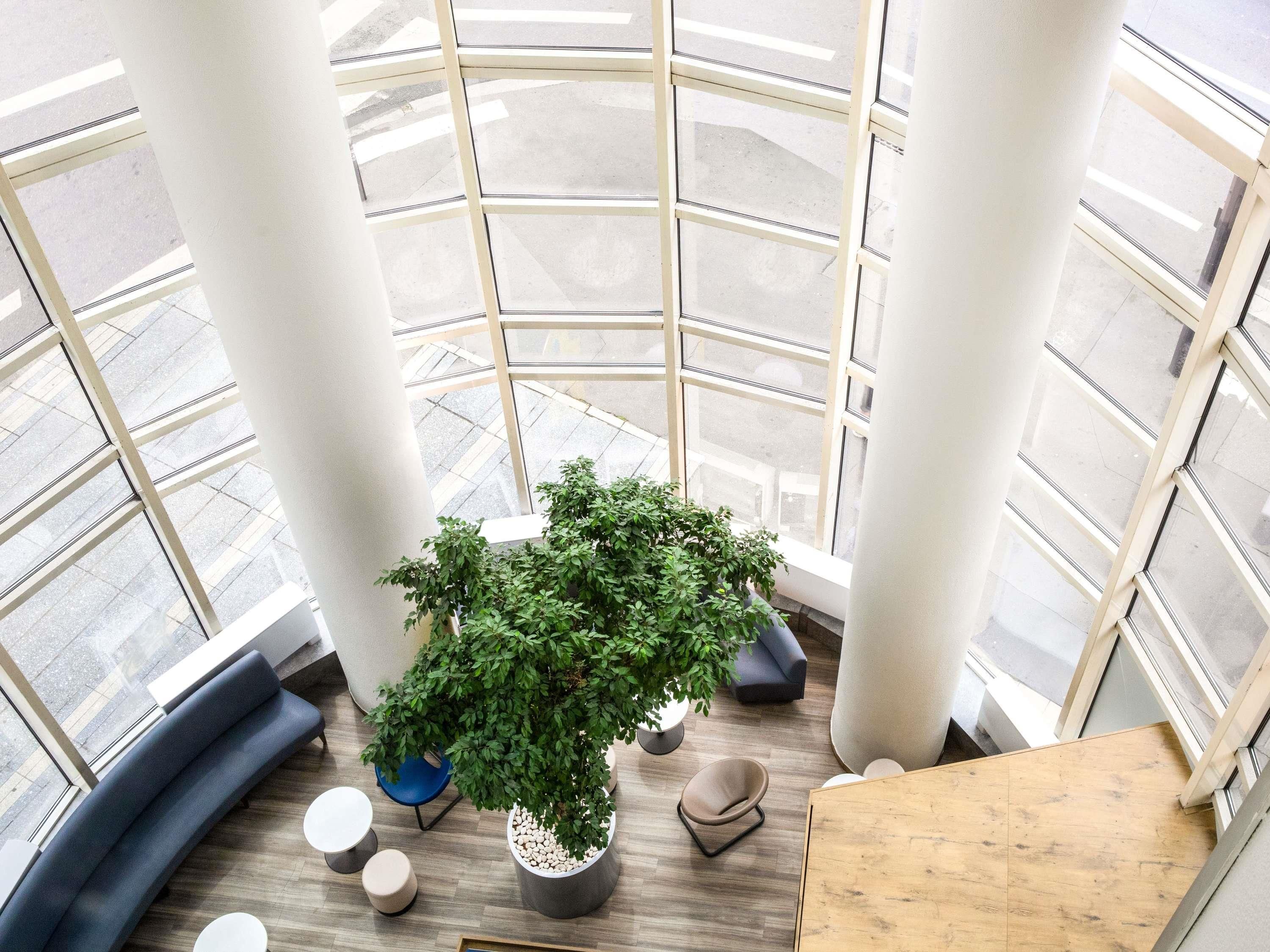 A modern interior with a large potted plant, seating areas, and a view through a glass atrium.