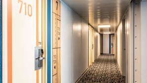 A hotel hallway with numbered doors, a patterned floor, and a light fixture on the ceiling.