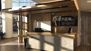 A reception desk with a wooden counter and a glass partition, a sign reading "RECEPTION", and a view of the street outside. - ibis budget Paris Porte de Montreuil (Montreuil)