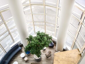 Un intérieur moderne avec un grand atrium vitré, une plante en pot placée au centre et un mobilier contemporain.