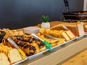 Una mesa de bufé con panes, pasteles y un pequeño bol blanco.