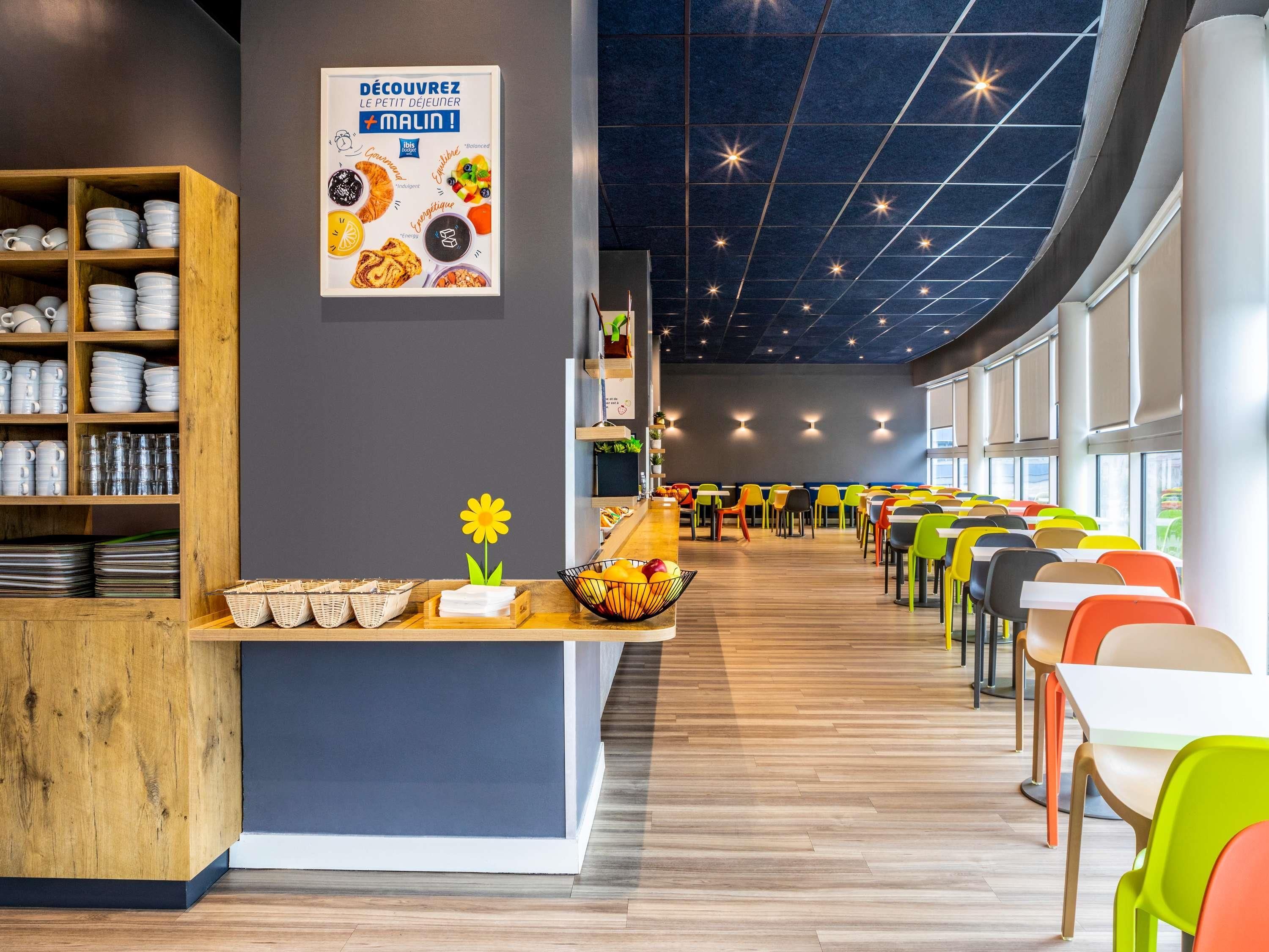 Um café moderno com prateleiras de madeira, cadeiras coloridas e um letreiro anunciando um pequeno-almoço.