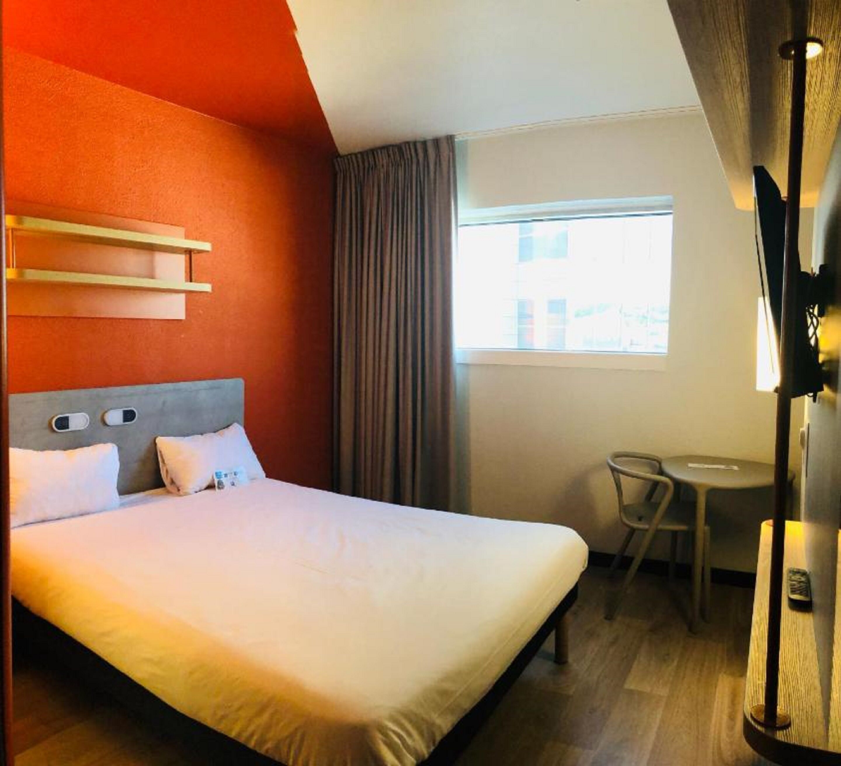 Ein Hotelzimmer mit einem Bett, einem kleinen Tisch, einem Stuhl und einem Fenster mit Vorhängen.