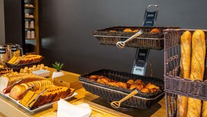 A buffet table with various breads, pastries, and a knife on a cutting board.