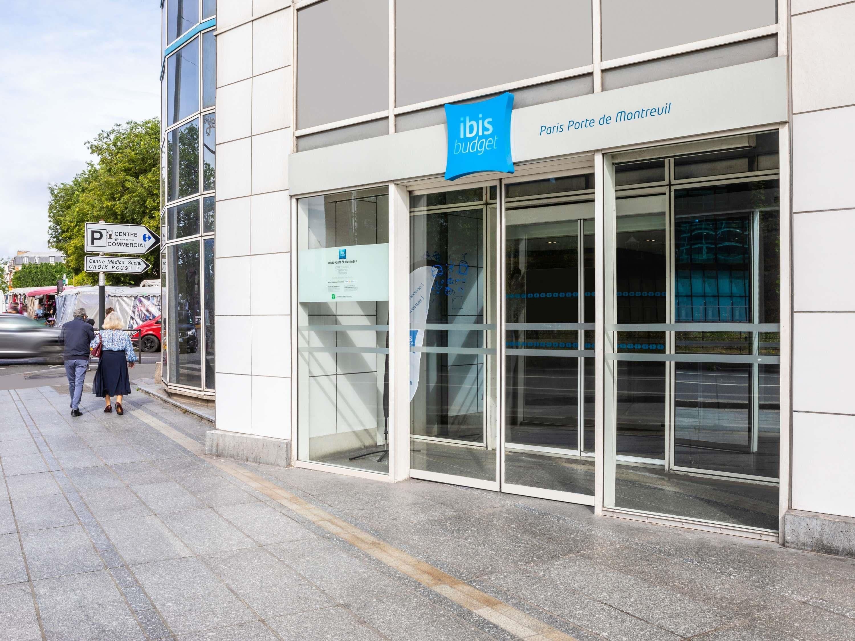 A modern building with a glass facade, a blue sign for ibis budget, and a sign indicating a commercial parking area.