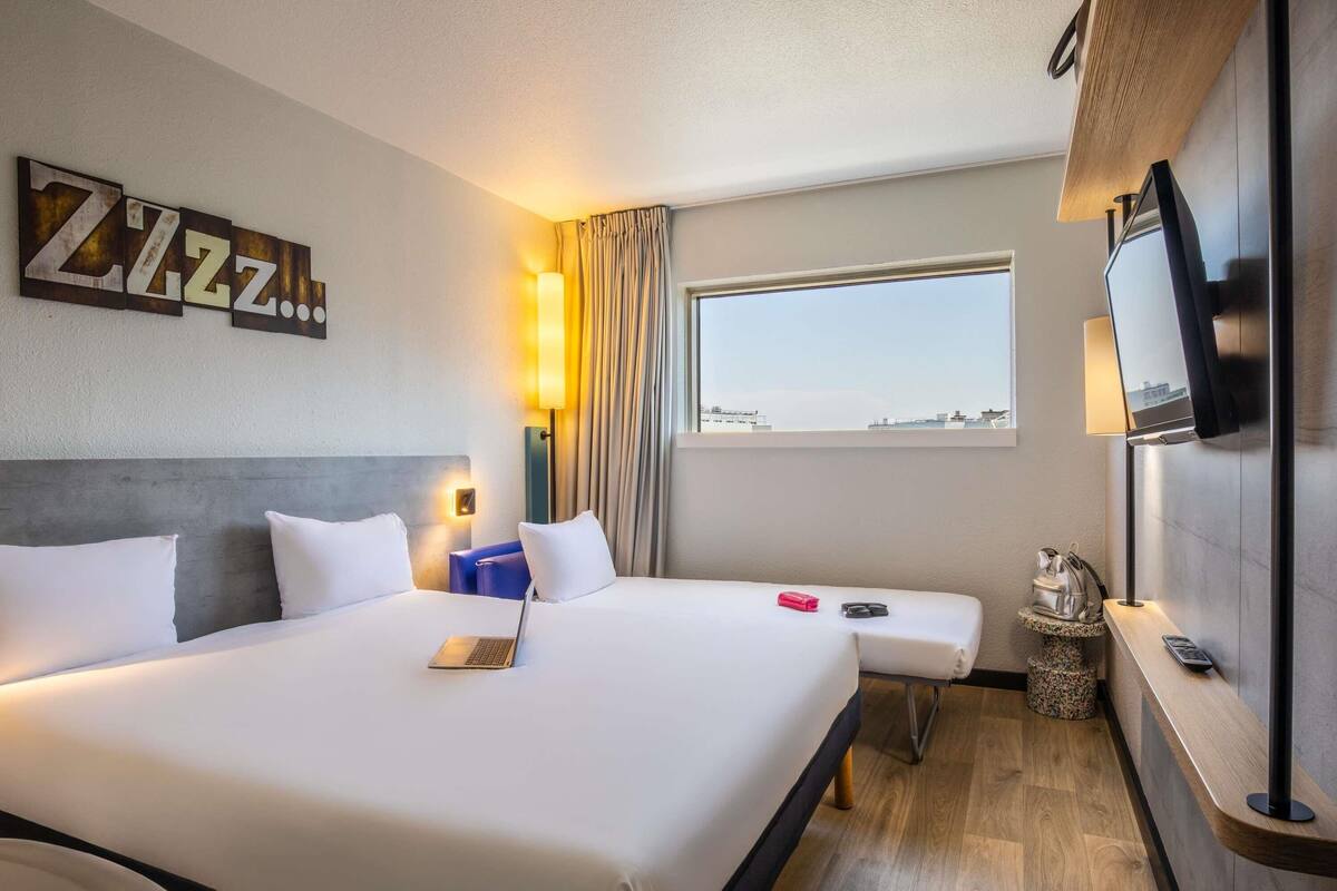 A hotel room with a large bed, a desk, a TV, and a window with a city view.
