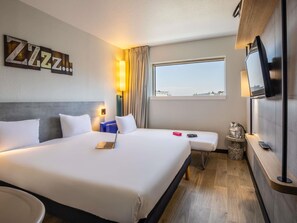 Habitación de hotel con una cama grande, un escritorio, un televisor y una ventana con vista a la ciudad.
