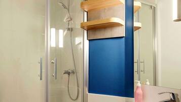 A modern bathroom with a glass shower enclosure, a white sink, and wooden shelves above the mirror.