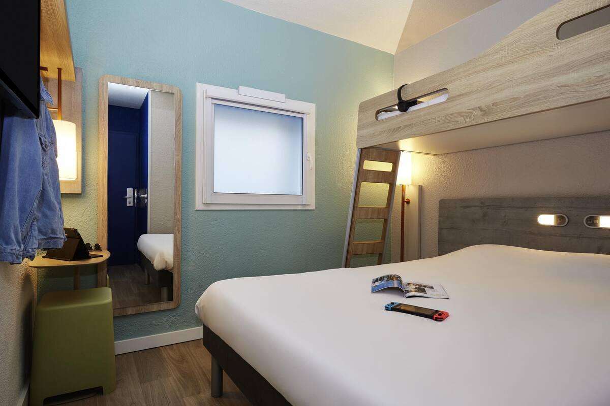 Una habitación de hotel con cama, mesita de noche, espejo, ventana y puerta.