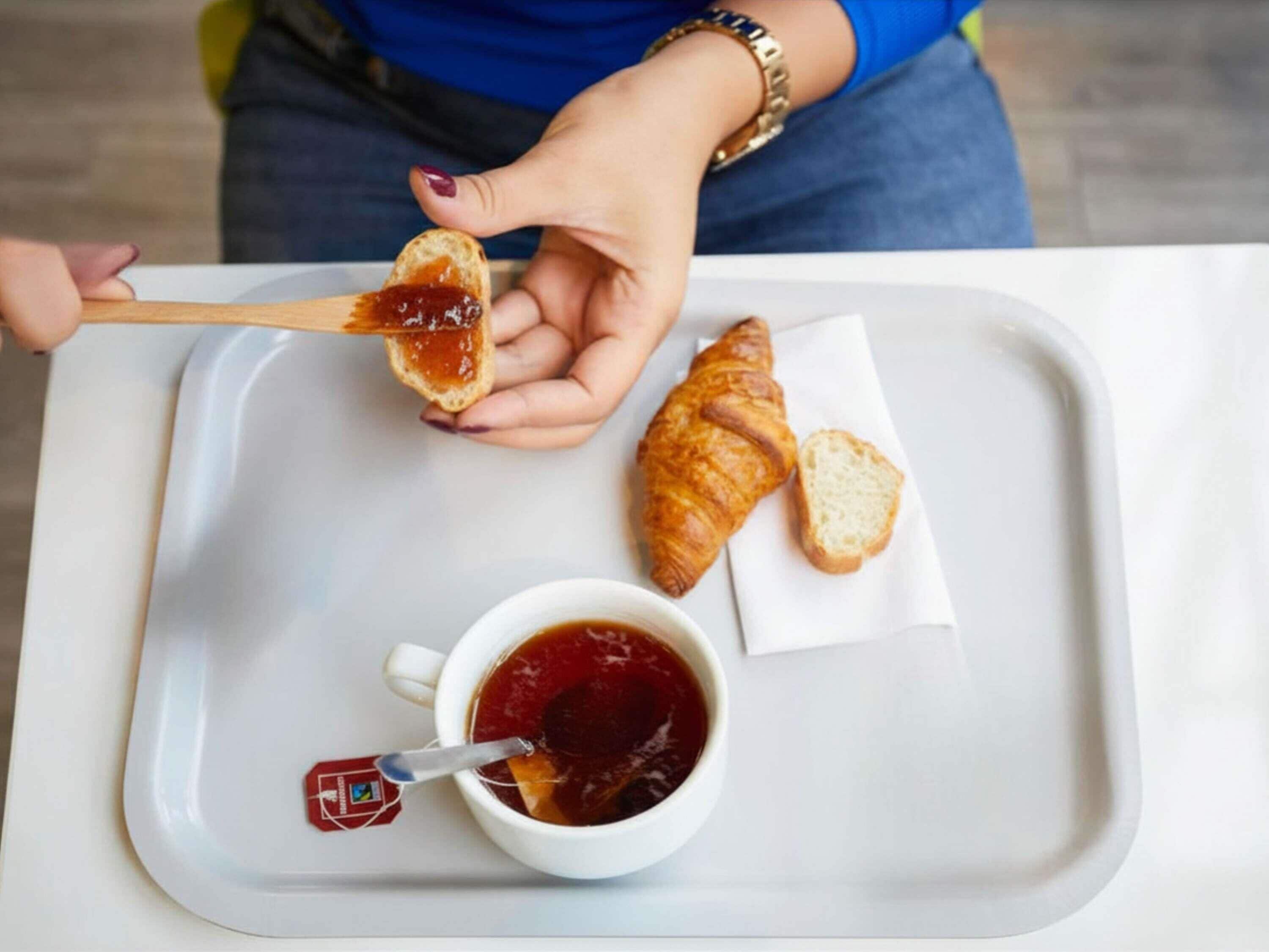A tray with a croissant, a slice of bread with jam, and a cup of tea.