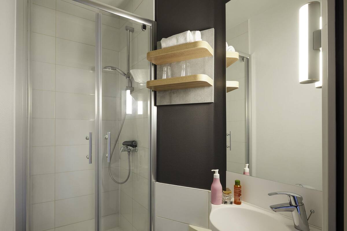 Une salle de bain moderne avec une douche à parois de verre, un lavabo blanc et un miroir au-dessus du lavabo.