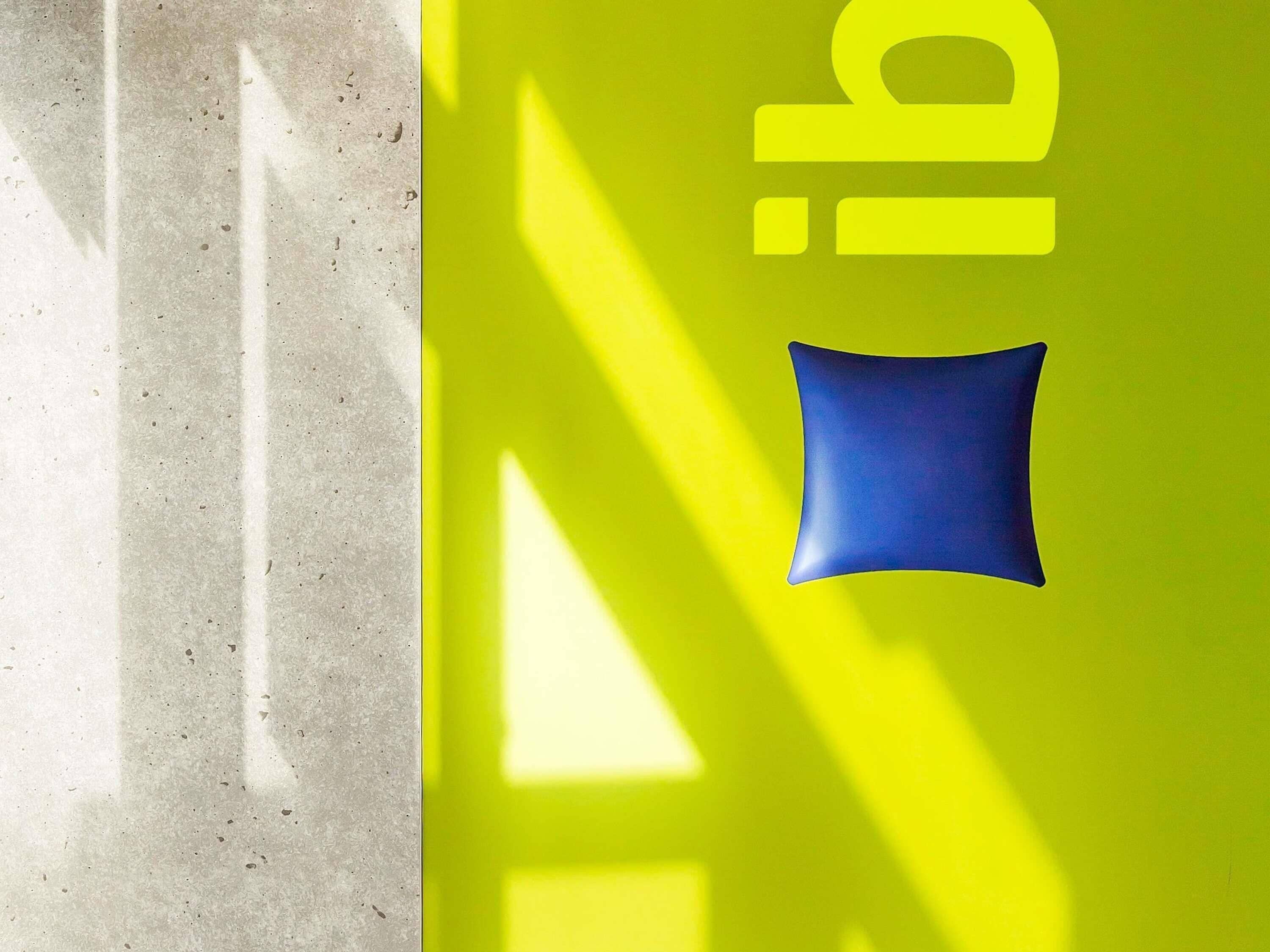 A bright yellow wall with a blue square and the text 'iib' in white.