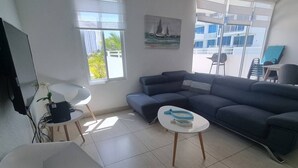 Una sala de estar moderna con un sofá modular, una mesa de centro blanca, un televisor y un cuadro de veleros.