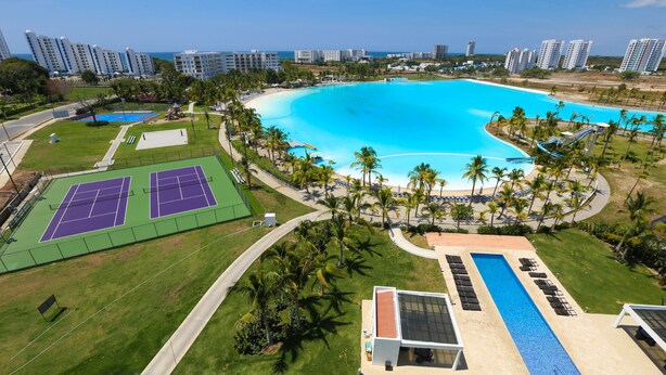 Una gran piscina rodeada de palmeras y canchas de tenis, con rascacielos al fondo.