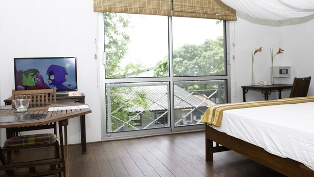 A bedroom with a large window, a bed, a desk with a computer, and a chair. - Boom Apartments (Paramaribo)