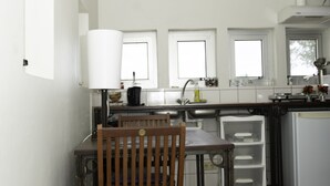 A kitchen with a wooden chair, a table, a refrigerator, and a window. - Boom Apartments (Paramaribo)