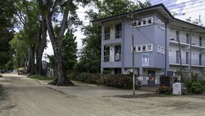 A multi-story building with balconies, a dirt road in front, and trees. - Boom Apartments (Paramaribo)