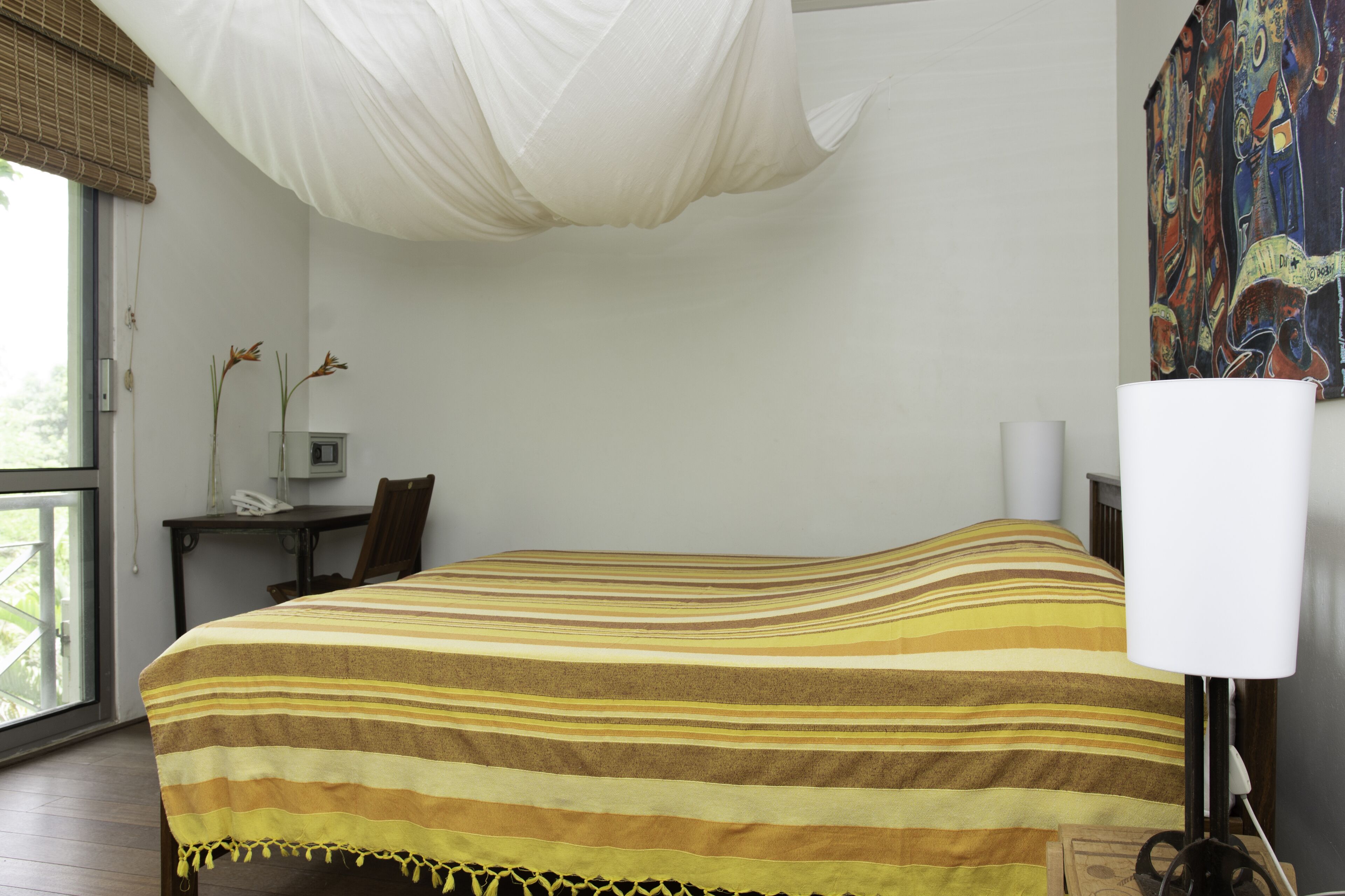 Habitació d'hotel amb un llit, una taula de treball, una cadira, una làmpada i un quadre a la paret.